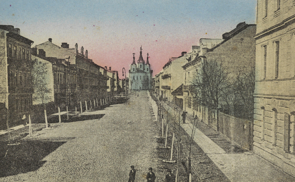 Przedwojenna, koloryzowana pocztówka prezentuje ulicę, której obie pierzeje są zabudowane kamienicami i obsadzone młodymi drzewami. Oś ulicy zamyka trójwieżowa świątynia.