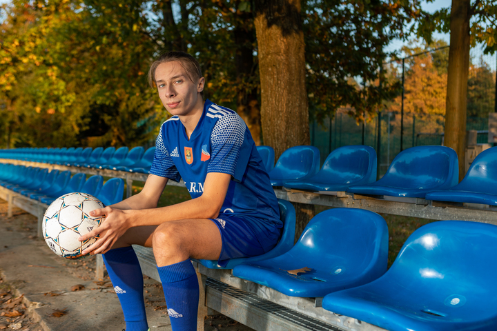chłopak w stroju sportowym z piłka w ręku siedzi na trybunach boiska piłkarskiego